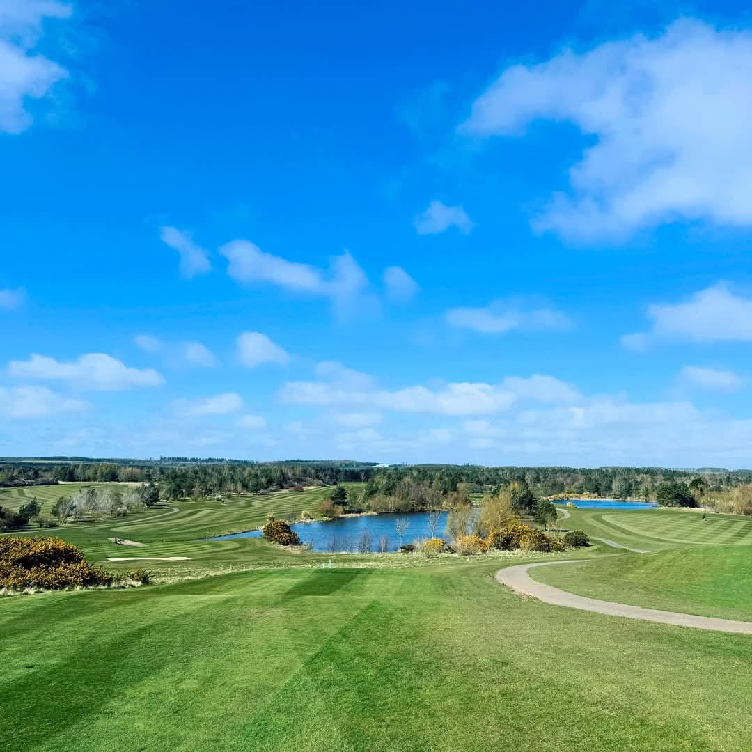 Lush green golf course with a pond and blue sky